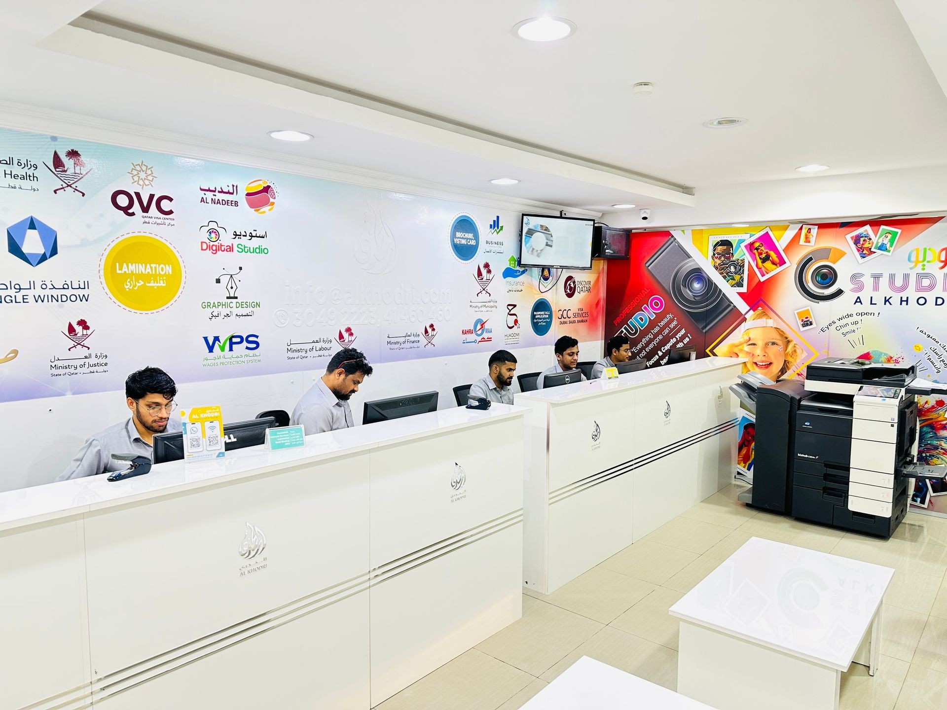 Office reception area with staff working at computers and colorful wall graphics featuring logos and designs.