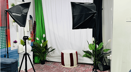 Photography studio setup with lighting equipment, plants, and a white backdrop.