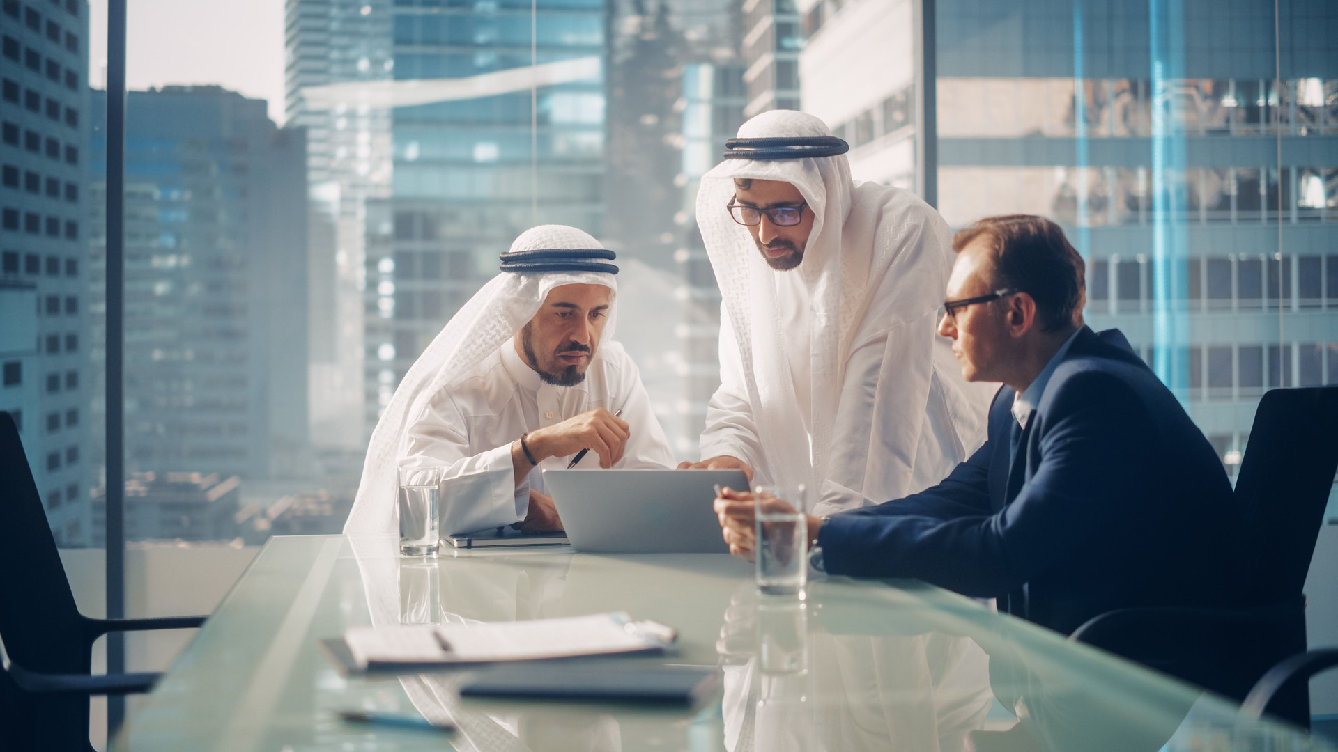 International Business Consultant Advises on Financial Strategy Plan to Successful Arab Company Owners. Multicultural Meeting in Modern Office Between American and Saudi Businessman.